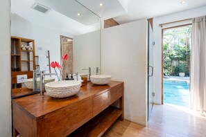 Casa de banho com duas pias redondas e texturizadas, toucador de madeira, um espelho grande e porta de vidro para uma piscina.