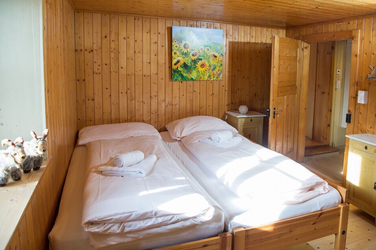 Habitación de cabaña de madera con dos camas, un cuadro de girasoles y una mesita con una lámpara.