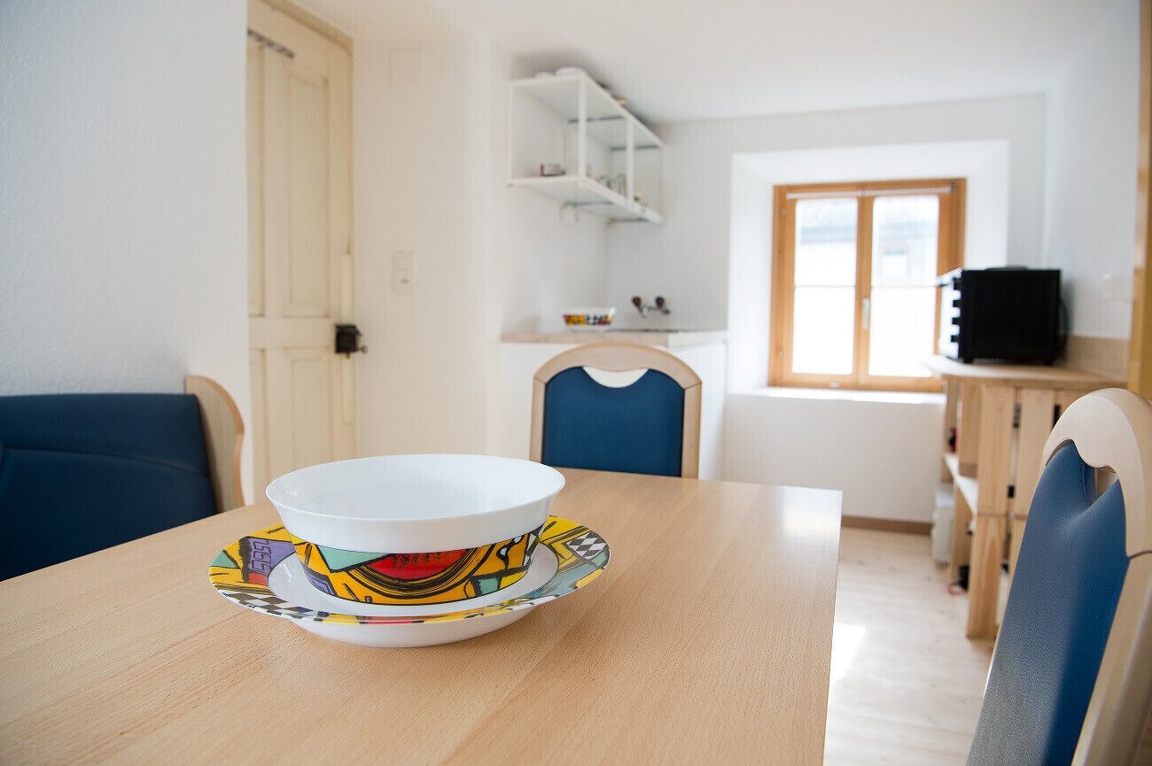 A dining area with a table set for two, a blue chair, and a white bowl with a colorful design on the table.