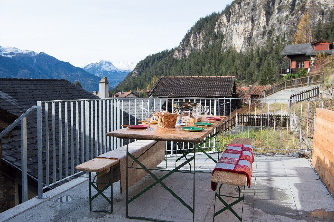 Een terras met een eettafel, een bankje en uitzicht op bergen.