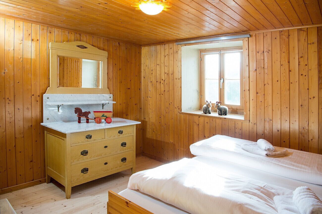 Une pièce aux murs lambrissés, comprenant un lit, une commode, un miroir et une fenêtre.
