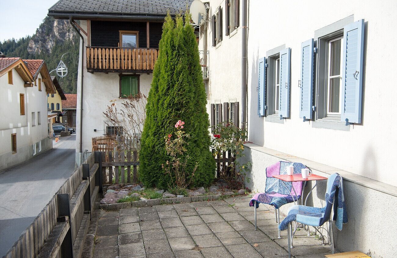 A narrow street with a small garden area, a wooden fence, and a table with chairs.