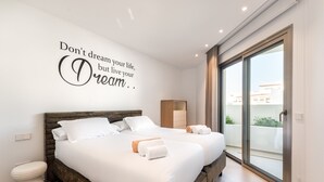 Une chambre d’hôtel moderne avec un grand lit, une petite table de chevet, une armoire et une porte-fenêtre coulissante donnant sur le balcon.