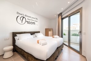 Une chambre d’hôtel moderne avec un grand lit, une petite table de chevet, une armoire et une porte-fenêtre coulissante donnant sur le balcon.
