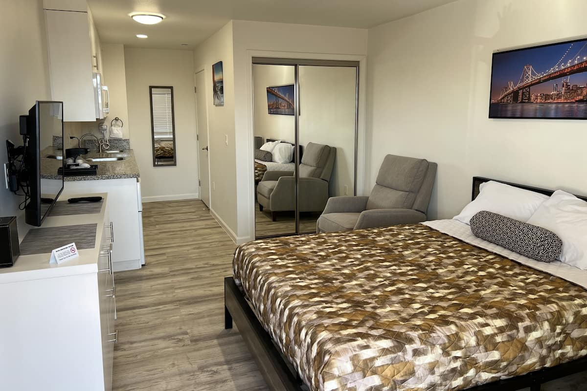 A hotel room with a bed, a desk with a computer, a chair, a mirror, and a painting of a bridge.