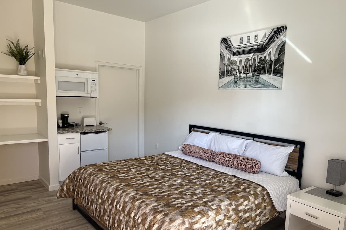 A bedroom with a bed, a nightstand, a white wardrobe, a microwave, and a coffee maker.