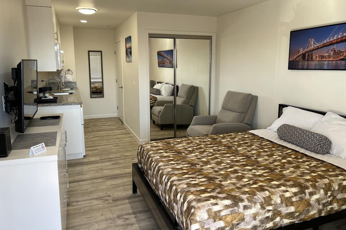 A hotel room with a bed, a desk with a computer, a chair, and a large mirror.
