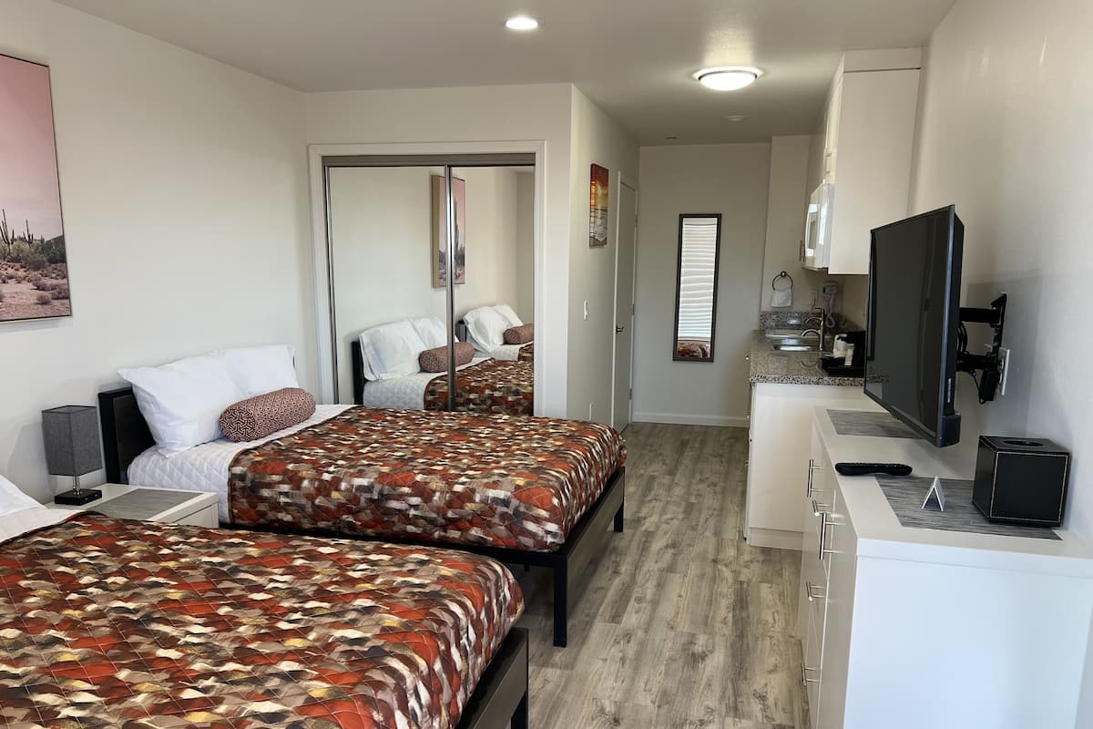 A hotel room with two beds, a TV, a desk, and a bathroom visible through a door.