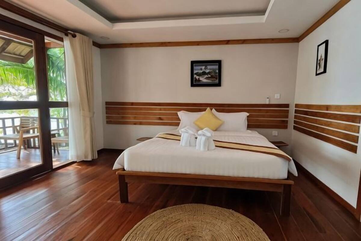 A hotel room with a large bed, wooden headboard, and a view through a glass door to an outdoor area.