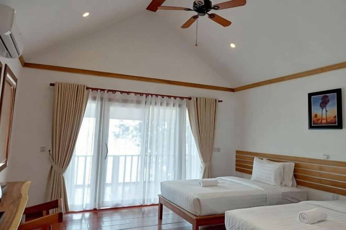 A bedroom with two beds, a ceiling fan, and a large window with curtains.