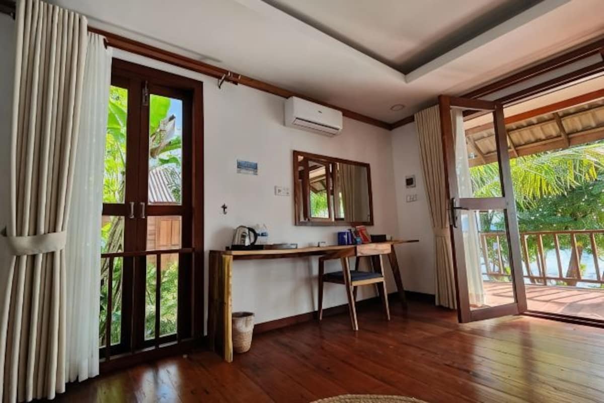 A room with a wooden floor, a desk with a chair, a window, and an air conditioning unit.