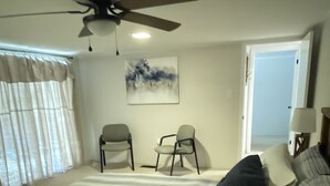 Ein Schlafzimmer mit einem großen Bett, zwei Sesseln, einem Deckenventilator und einer Tür zu einem anderen Raum.