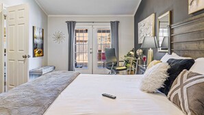 Habitación de hotel con cama, escritorio, silla, ventana con cortinas y puerta.