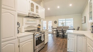 Una cocina con armarios blancos, estufa y comedor con mesa y sillas.