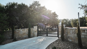 A gated driveway leading to a building with stone walls and a clear sky. - Hill Country Farmhouse Near Canyon Lake + Wineries (Fischer)
