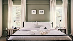 A neatly made bed with white linens and pillows, two bedside tables with lamps, and two framed pictures on the wall. - Hill Country Farmhouse Near Canyon Lake + Wineries (Fischer)
