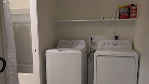 Un área de lavandería con dos lavadoras blancas, un estante con productos de limpieza y una cortina de ducha.