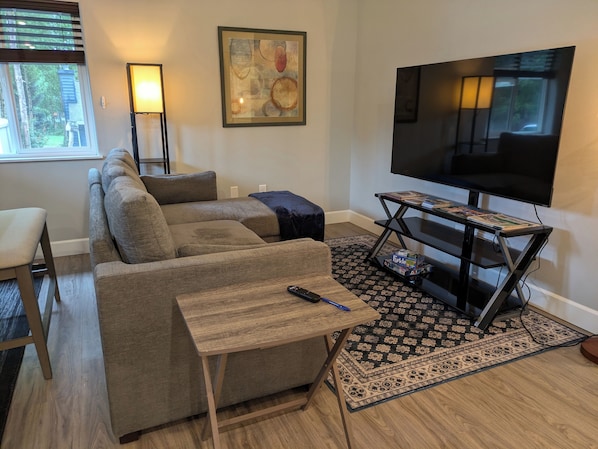 Una sala de estar con un sofá modular, un televisor sobre un mueble bajo, una mesita y una alfombra estampada.