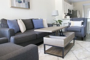 A modern living room with a grey sofa, a wooden coffee table, and a grey armchair. - Serenity in Heart of DFW w/ PRIVATE parking & KING Bed ⭑ Min. from DFW Airport + (Euless)