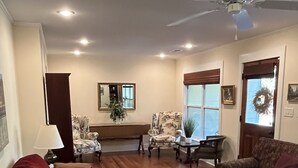 A spacious living room with a red sofa, patterned armchairs, a large rug, and a ceiling fan.