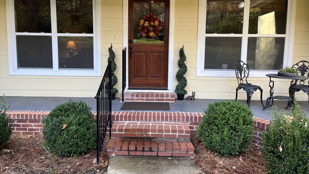 A house with a front door, two windows, a small porch, and a potted plant.
