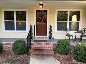 A house with a front door, two windows, a small porch, and a potted plant.