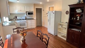 A kitchen with white cabinets, a microwave, a refrigerator, and a dining area with a wooden table and chairs.