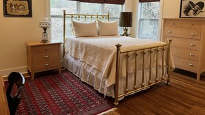 A bedroom with a bed, nightstands, a dresser, a ceiling fan, and a window with a view of trees.