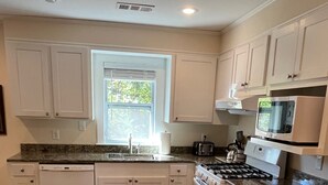 A kitchen with white cabinets, a granite countertop, a window, and a microwave.