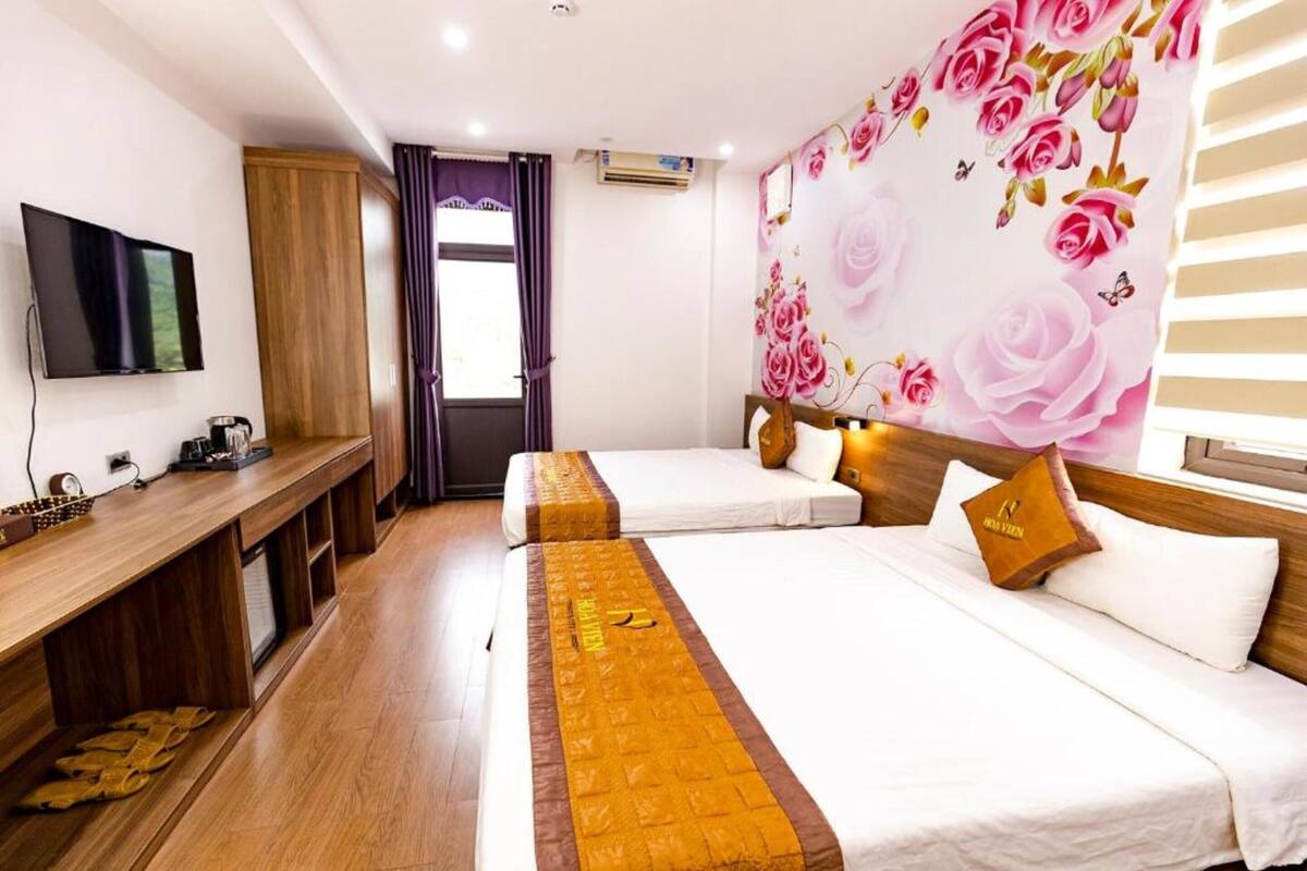 Une chambre d’hôtel avec deux lits, un bureau en bois, un téléviseur à écran plat et une décoration murale à motifs floraux.