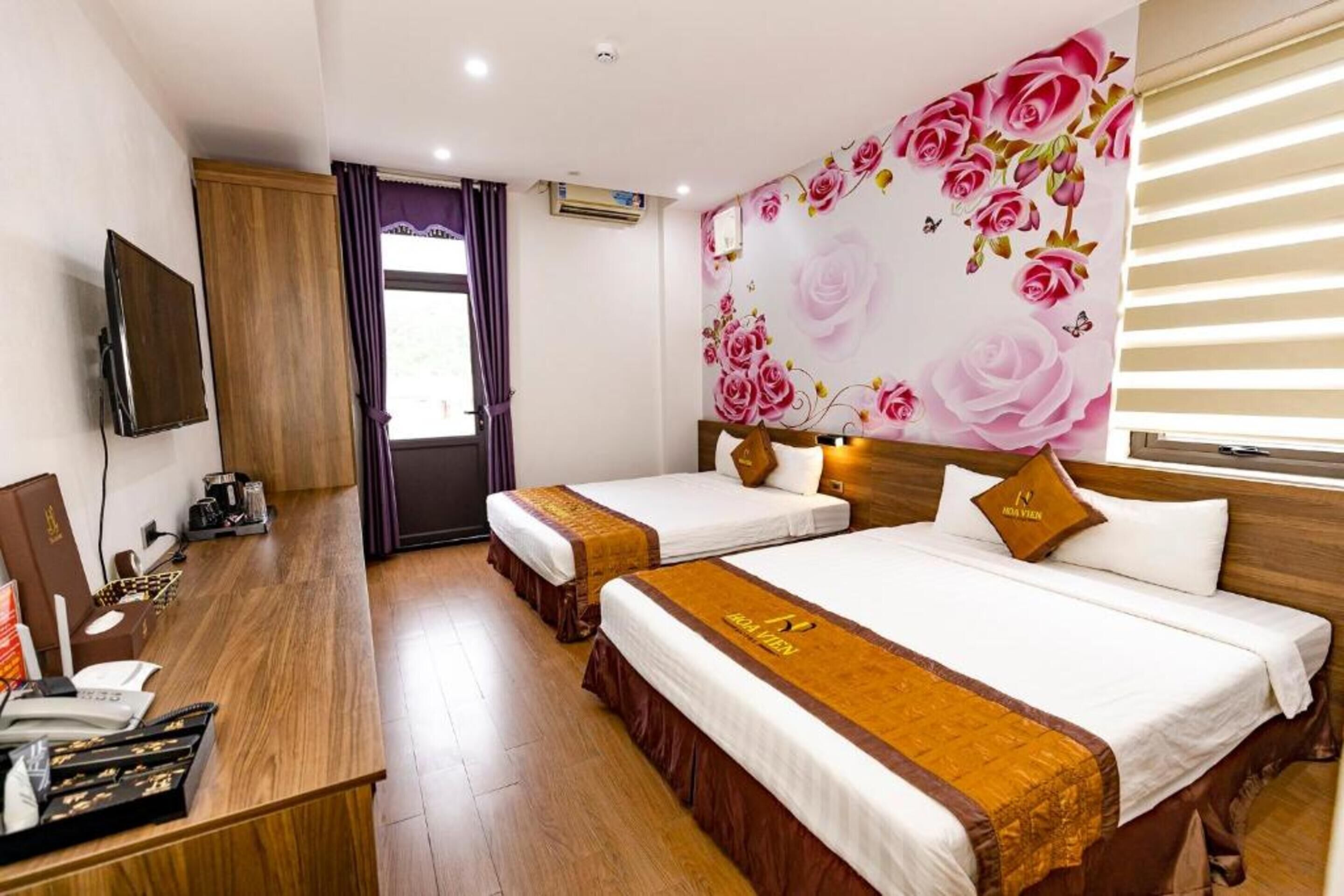 Habitació d'hotel amb dos llits, un escriptori amb ordinador i telèfon, i una paret amb un mural floral.
