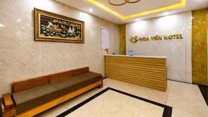 A hotel reception area with a marble floor, a wooden reception desk, a sofa, and a framed artwork on the wall.