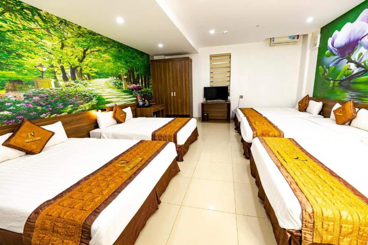 Une chambre d’hôtel avec quatre lits, une télévision, une armoire et une fresque représentant une forêt.