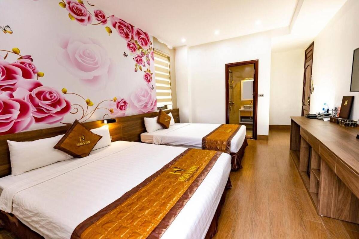 Une chambre d’hôtel avec deux lits, une tête de lit en bois, une décoration murale à motifs floraux, un bureau en bois et un miroir.