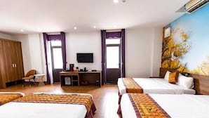 A hotel room with two beds, a desk with a computer, a TV, and a large window with curtains.