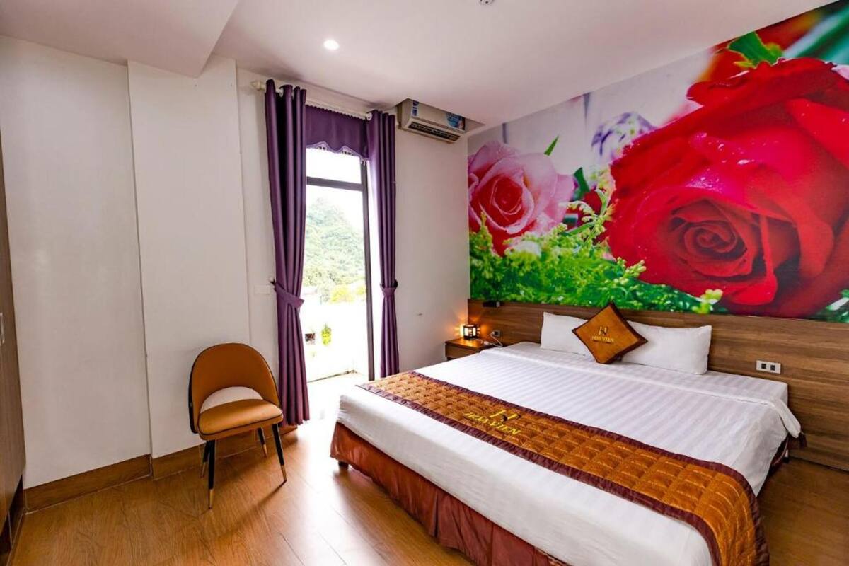 Une chambre d’hôtel avec un lit, une chaise, une grande fenêtre avec des rideaux et une fresque murale représentant des roses.
