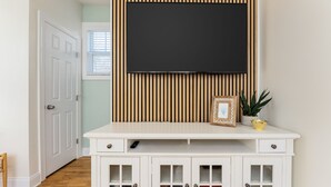 Una habitación con un mueble blanco para entretenimiento, un televisor montado y un armario con puertas de vidrio.