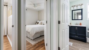 Un dormitorio con cama, ventilador de techo, mesita de noche y cómoda con espejo.