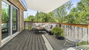 A wooden deck with outdoor furniture, including a sofa and chairs, and a large umbrella providing shade.