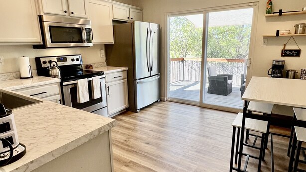A modern kitchen with white cabinets, stainless steel appliances, and a wooden floor.
