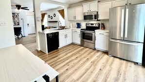 A modern kitchen with white cabinets, stainless steel appliances, and a wooden floor.