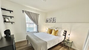A bedroom with a bed, bedside tables, a dresser, a window with curtains, and wall art.
