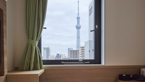 Una habitación con ventana que ofrece vistas a un paisaje urbano, destacando una torre imponente.