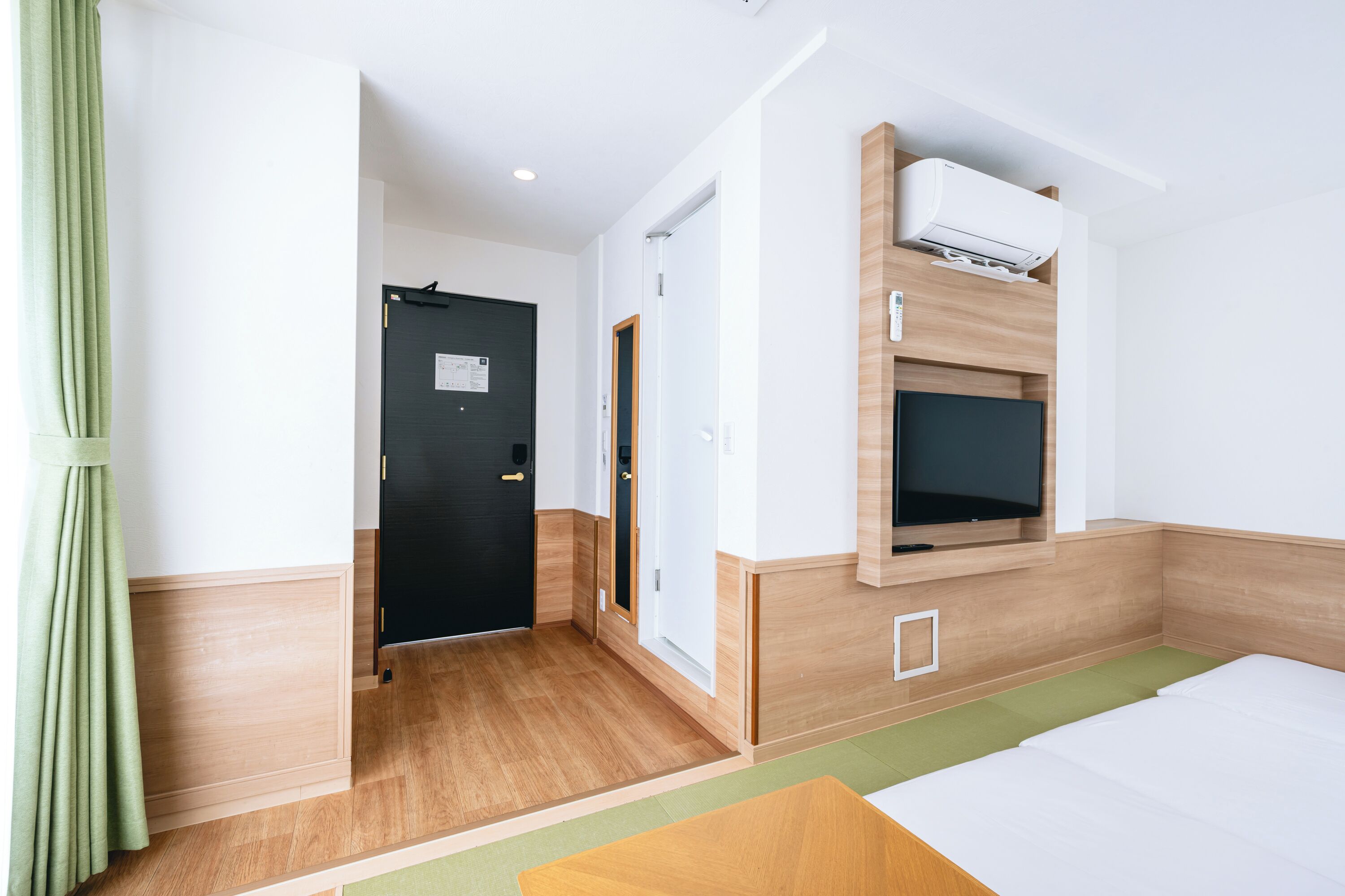 Una habitación de hotel con cama, televisión montada en la pared, una puerta y un equipo de aire acondicionado.