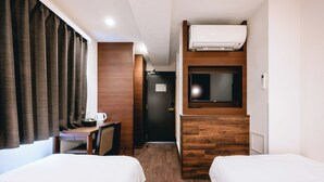 Habitación de hotel con dos camas, un escritorio con silla, televisor y aire acondicionado.