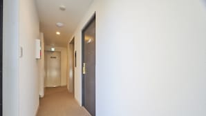 Un pasillo con piso alfombrado, una puerta con manija de latón y una lámpara fijada en la pared.