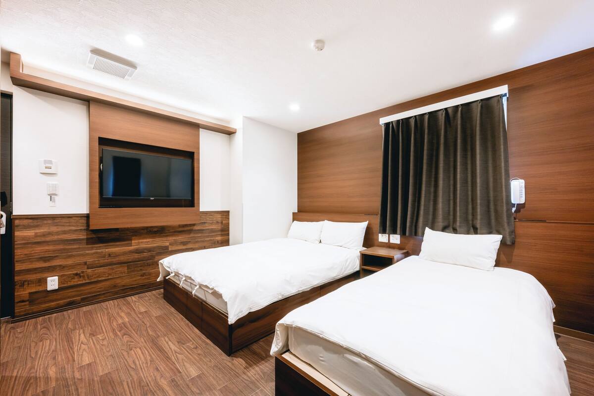 A hotel room with two beds, a TV mounted on the wall, and a window with curtains.