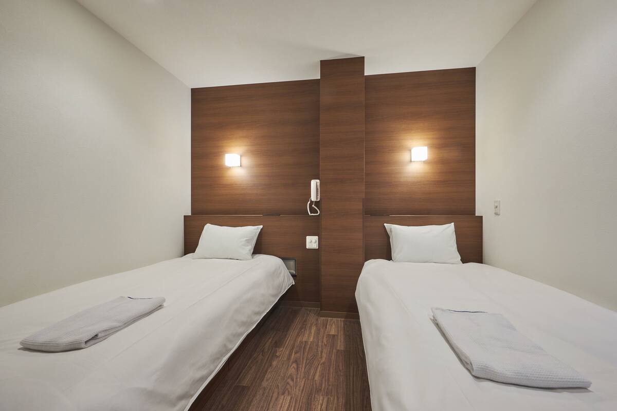 A hotel room with two single beds, wooden headboards, and bedside lamps.