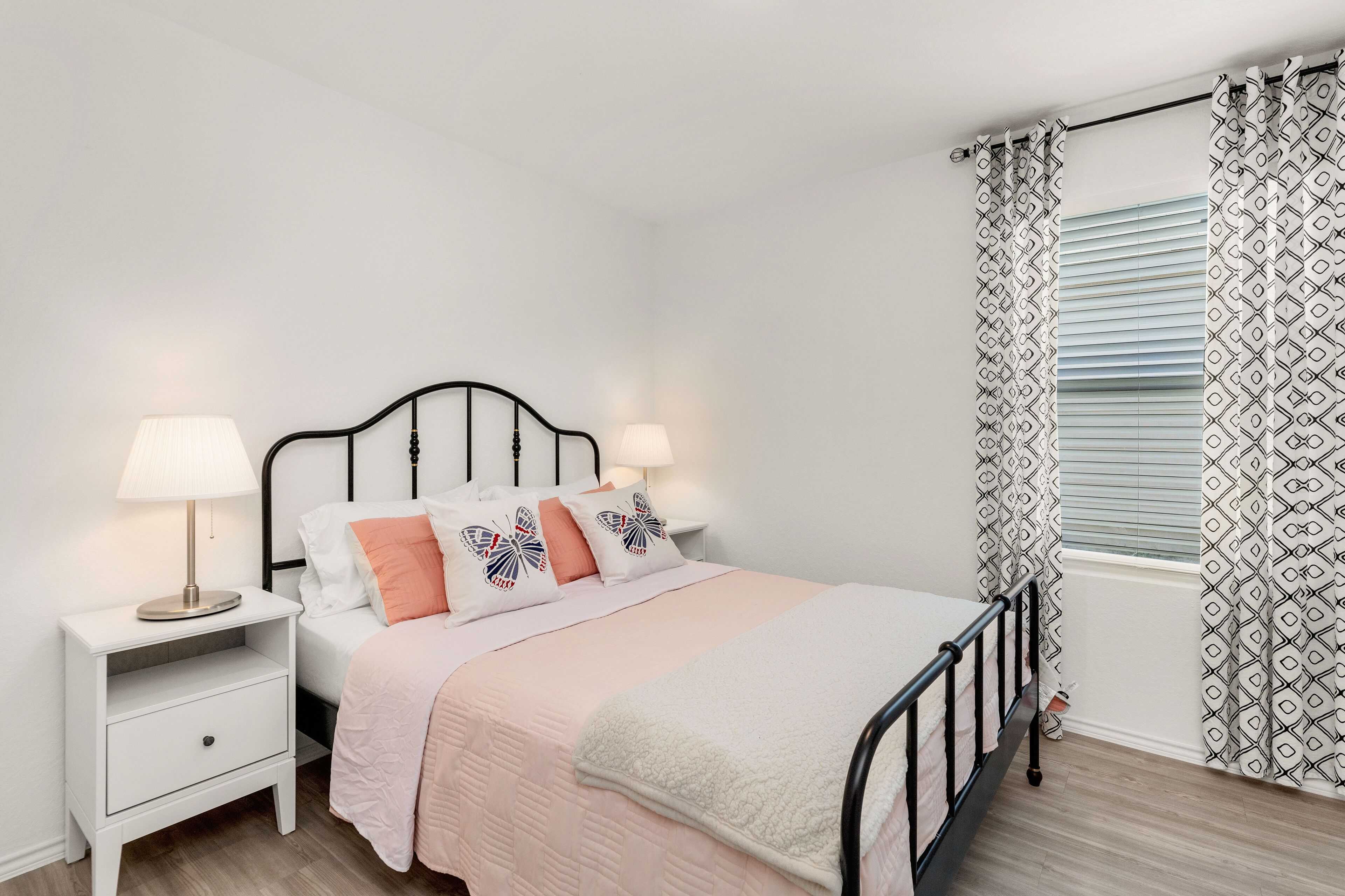 A neatly arranged bedroom with a single bed, a bedside table with a lamp, and patterned curtains.