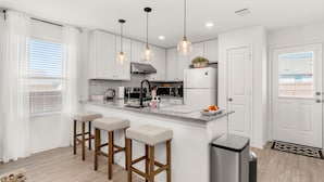 A modern kitchen with white cabinets, a stainless steel refrigerator, a gas stove, and three bar stools.